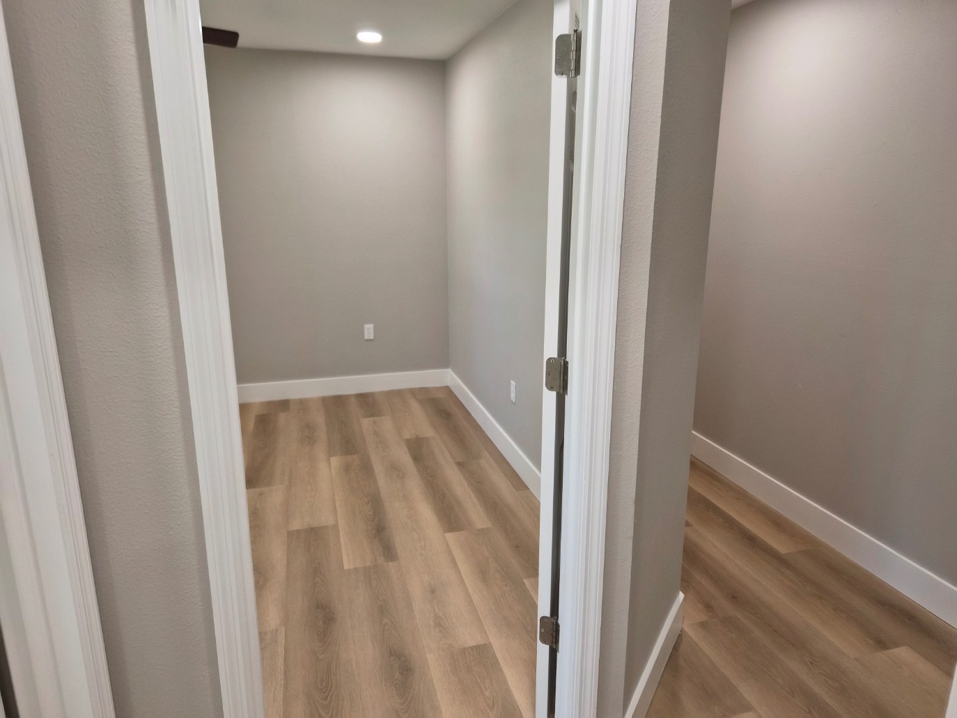A small, empty room with light wood flooring and light gray walls, viewed through an open white door. The room is brightly lit by recessed ceiling lights—ideal for your next Pensacola remodeling or home construction project.