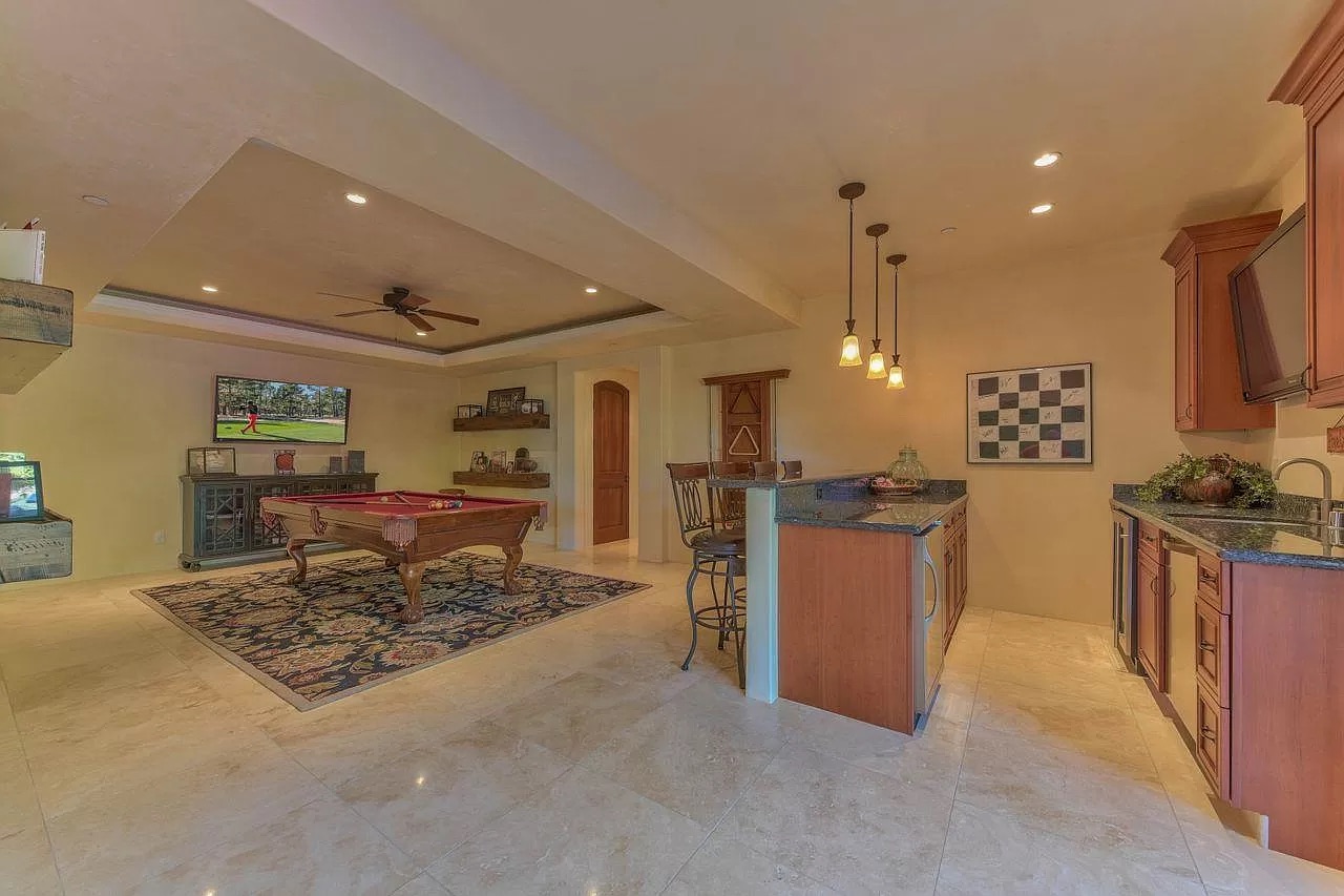 Spacious game room and kitchenette, recently updated by a general contractor Pensacola, with pool table, TV, bar stools, granite countertops, pendant lights, decorative rug on tiled floor. Wall art and cabinets add to the cozy atmosphere.