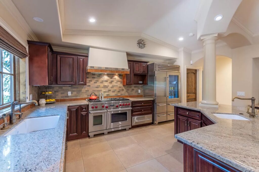 Spacious modern kitchen with granite countertops, dark wood cabinets, stainless steel appliances, a large stove, farmhouse sink, tiled backsplash, and natural light—perfect for your next Pensacola remodeling or kitchen remodel project.