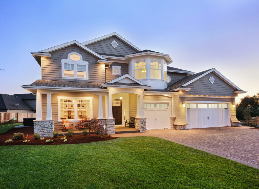 A large, modern two-story house in Pensacola with a manicured lawn, stone accents, and warm exterior lighting at sunset. Perfect for those considering a kitchen remodel or bathroom remodel by an experienced general contractor.