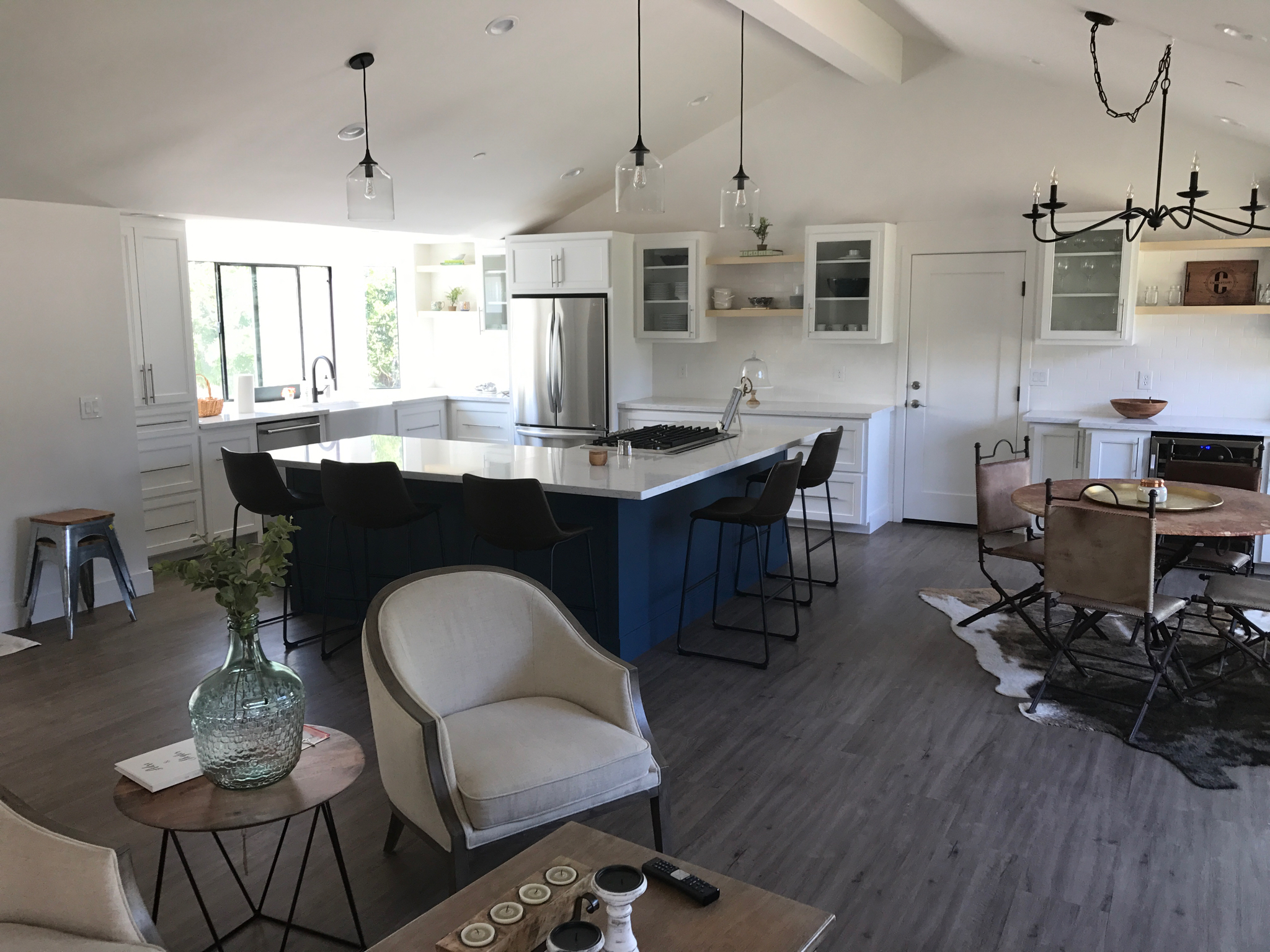 Modern open-concept kitchen and living area with white cabinets, a large island, stainless steel appliances, and a round dining table on a cowhide rug. Light wood flooring throughout—expertly finished by your trusted general contractor Pensacola.