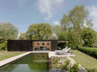 A modern black wood pool house with a shaded patio, outdoor sofa, and lounge chairs sits beside a natural swimming pool—showcasing the craftsmanship you'd expect from a Pensacola remodeling or general contractor Pensacola professional.